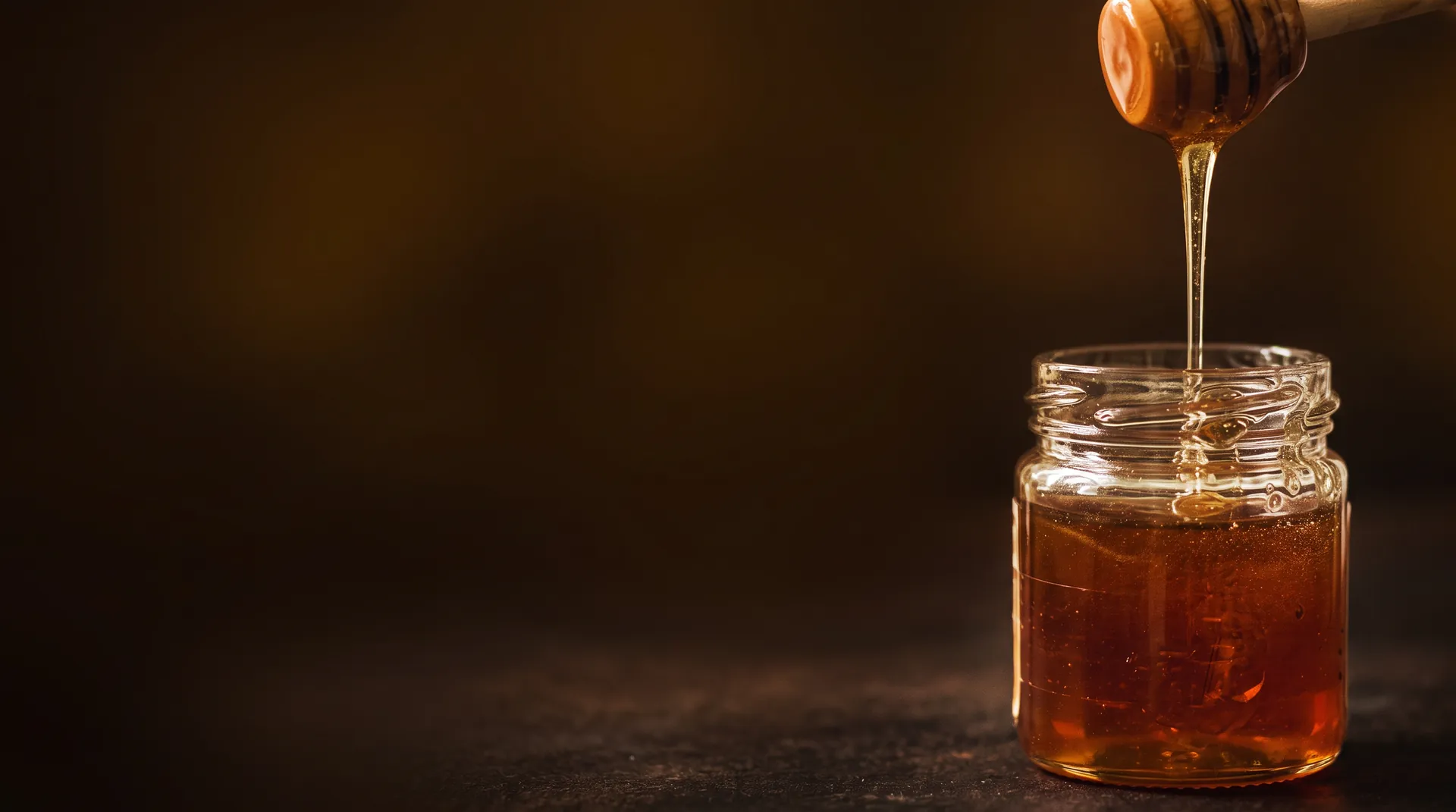 Hilo de miel cruda cayendo de una mielera de madera a un tarro de cristal
